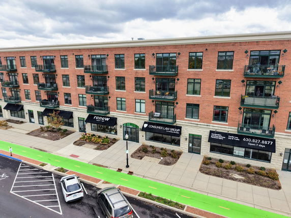 Front view of a multi-story brick building with balconies and retail spaces on the ground floor.