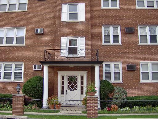 Front view of a multi-story brick apartment building with white shutters and a small entrance porch.
