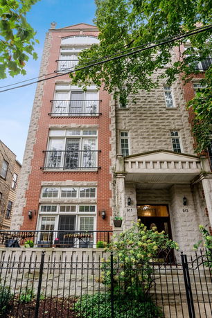 Front view of a multi-story residential building with balconies and a fenced entrance.