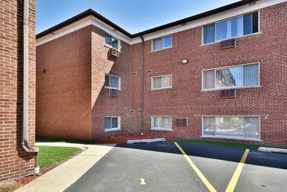 Front view of a three-story brick building with several windows and air conditioning units.