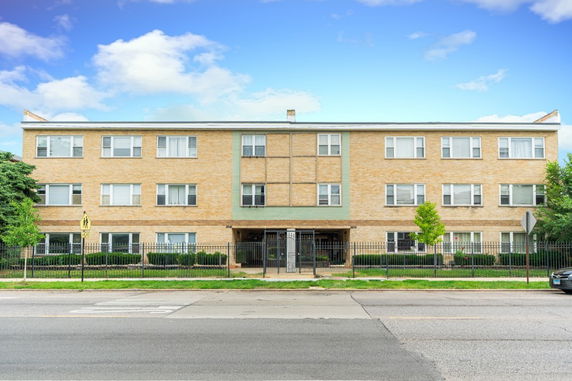 Front view of a three-story apartment building with a gated entrance and brick facade.