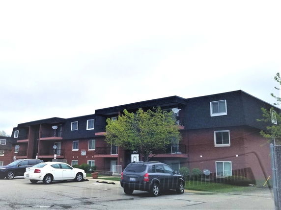 Front view of a multi-story apartment building with a parking area in front.