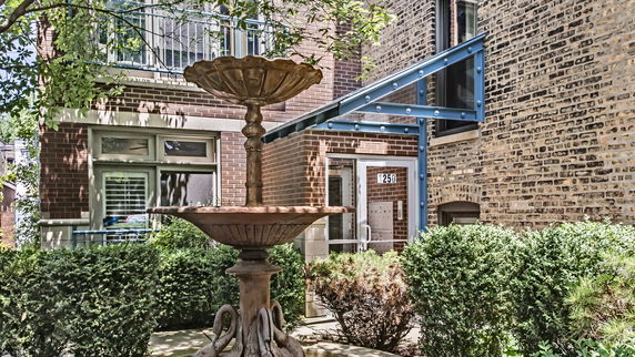 Front view of a brick building entrance with a metal awning and decorative fountain.