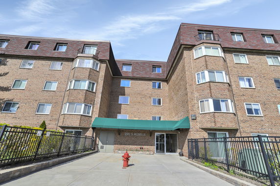 Front view of a multi-story brick apartment building with a green awning and numerous windows.