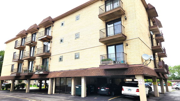 Front view of a multi-story apartment building with several balconies and covered parking area.