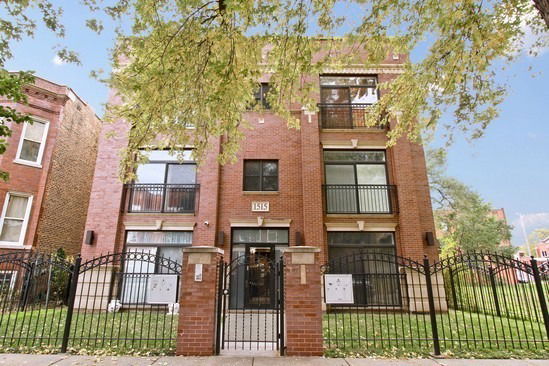Front view of a three-story brick apartment building with balconies and a gated entrance.