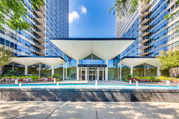 Front view of a modern building entrance with a distinctive roof design and a water feature in front.