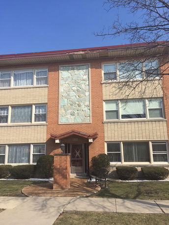 Front view of a three-story brick building with large windows and decorative stone panel.
