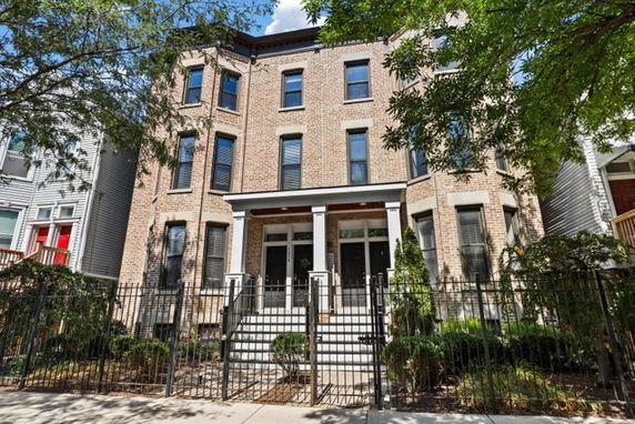 Front view of a three-story brick house with bay windows and a gated entrance.