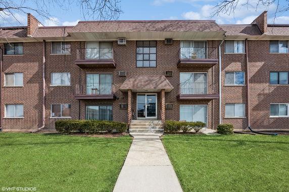 Front view of a three-story brick apartment building with balconies.