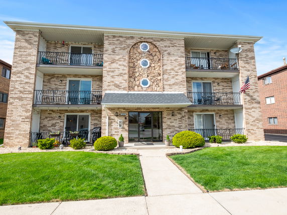 Front view of a three-story brick apartment building with balconies.