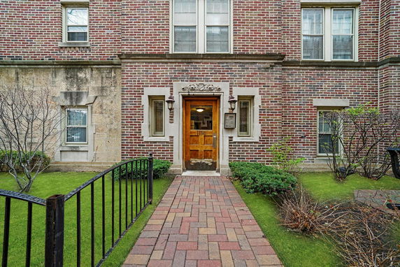 Front view of a brick building with a wooden door and decorative stone framing.