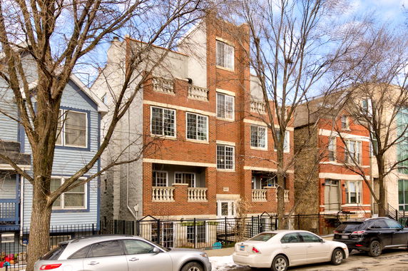 Front view of a brick apartment building featuring multiple floors and large windows.