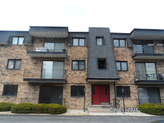 Front view of a three-story brick apartment building with balconies.