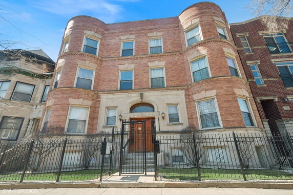 Front view of a three-story brick building with a fenced entrance.