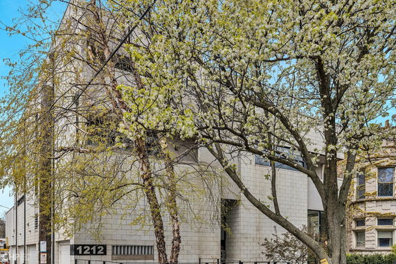 Front view of a multi-story building with modern architectural design and large trees in front.