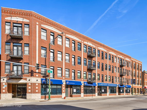 Front view of a multi-story brick building with commercial spaces on the ground floor and balconies on the upper levels.