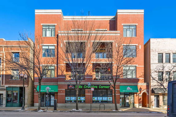Front view of a multi-story brick building with retail space on the ground floor.