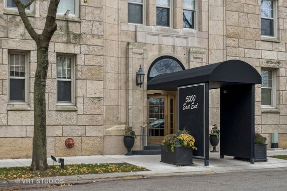 Front view of a stone facade building entrance with a black canopy and potted plants