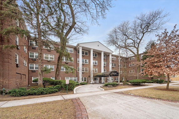 Front view of a multi-story brick apartment building with a columned entrance.