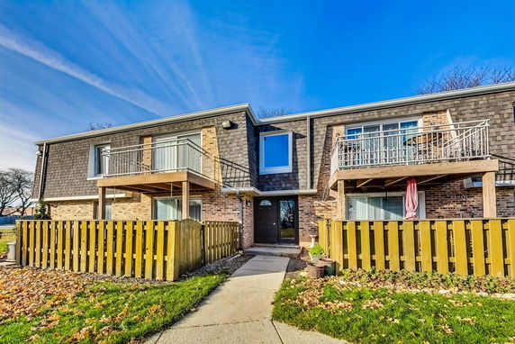 Front view of a two-story residential building with balconies and a wooden fence.