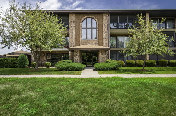 Front view of a three-story brick apartment building with large central window and covered entrance.