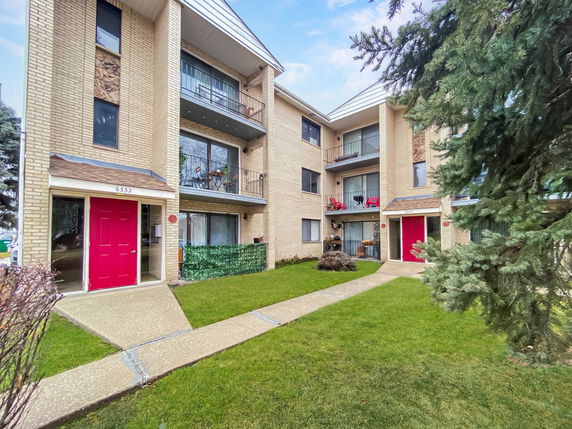 Front view of a three-story apartment building with balconies and red doors.
