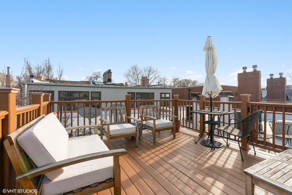 Rooftop deck with wooden chairs and a table, featuring an umbrella and a wooden railing.