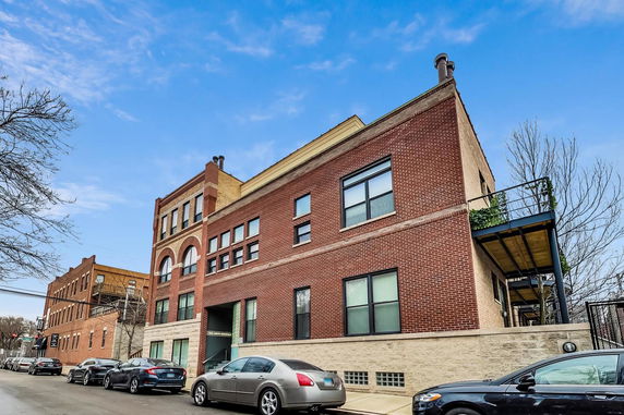 Front view of a brick multi-story building with large windows and a balcony.
