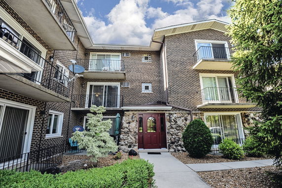 Front view of a multi-story brick apartment building with balconies and a central entrance.