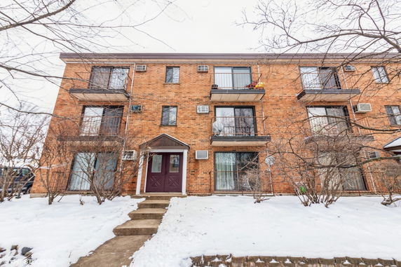 Front view of a three-story brick apartment building with balconies.