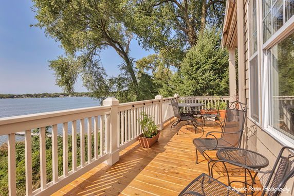 Wooden deck with metal furniture overlooking a lake and trees.