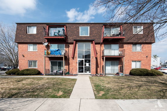 Front view of a three-story apartment building with brown roof and brick facade.