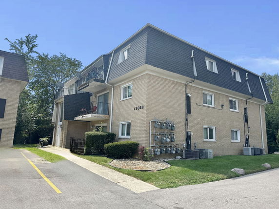 Street view of a multi-story apartment building with balconies and a sloped roof.