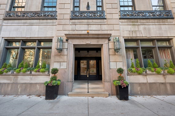 Front view of a building entrance with decorative plants and windows.