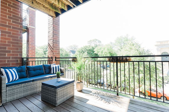 Outdoor seating area on a balcony with view of surrounding trees and buildings.