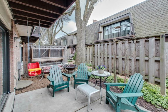 Outdoor patio area with chairs and a tree, adjacent to a building with a wooden fence.
