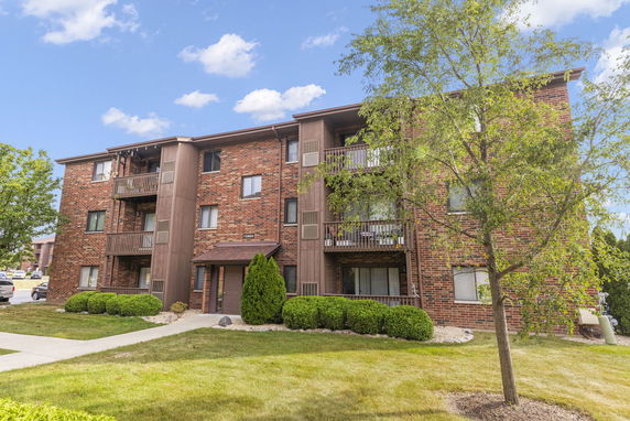 Front view of a three-story brick apartment building with balconies.