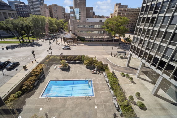 View of an outdoor swimming pool with surrounding patio area and adjacent buildings.