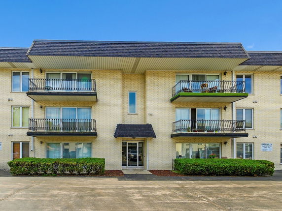 Front view of a three-story apartment building with balconies and brick exterior.
