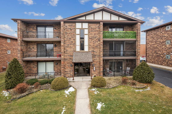 Front view of a three-story brick apartment building with balconies.
