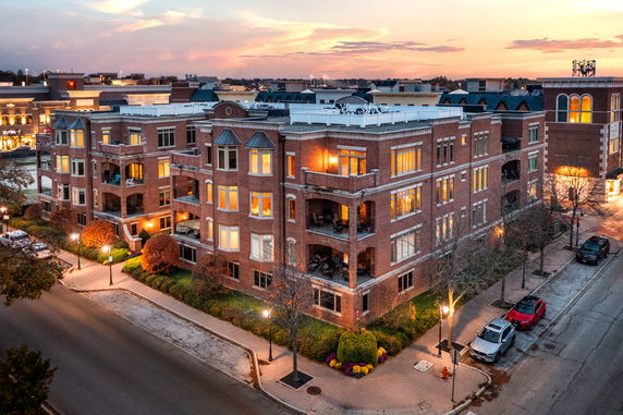 Elevated view of a large, multi-story brick apartment building with illuminated windows and balconies at sunset.