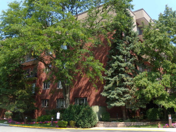 Front view of a multi-story brick building with balconies and trees surrounding it.