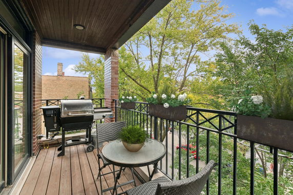 Balcony with outdoor furniture and a grill, overlooking surrounding area and trees.