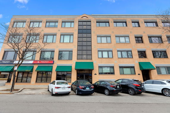 Front view of a four-story brick building with multiple windows and green awnings over the entrances.