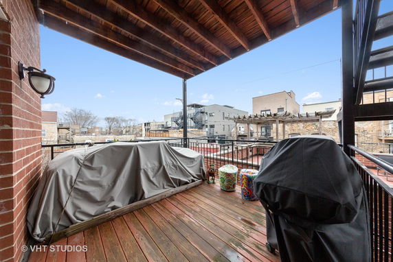 Wooden deck with covered furniture overlooking adjacent buildings and a pergola.