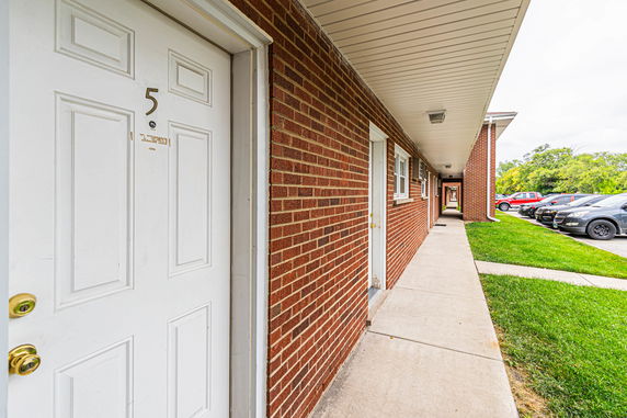 Exterior view of a building with a brick wall and multiple entry doors along a corridor.