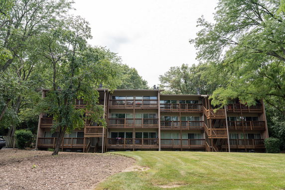 Front view of a multi-story building with balconies surrounded by trees.