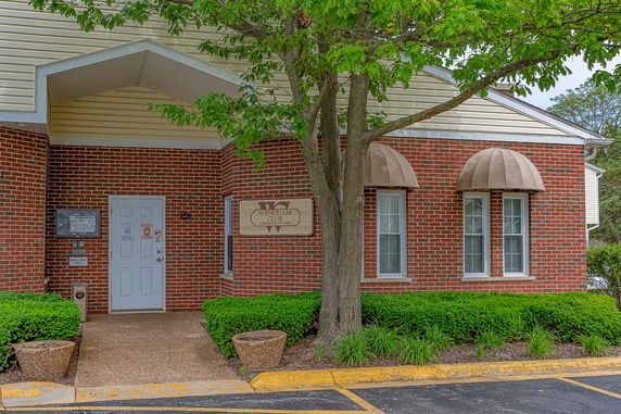 Front view of a brick building with a white door and two arched windows with awnings.