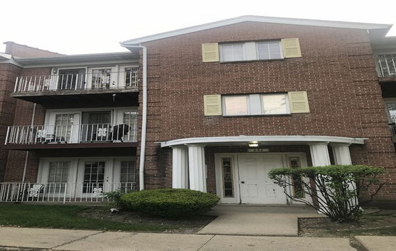 Front view of a three-story brick apartment building with balconies and a main entrance.